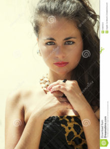 Beautiful teen portrait, italian female. Sunlit Portrait of an Italian girl. Dark hair, lipstick, hands close together, eyes bright sunbeams illuminate her right side (left in photo). Her look seems a gypsy. Gold necklace shining. Leopard topwear.