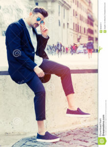Cool handsome fashion young man. Stylish man in the city A charming young stylish man with sunglasses. Sitting position, confident attitude with setting in the historic city of Rome, Italy. Fashionable clothes.