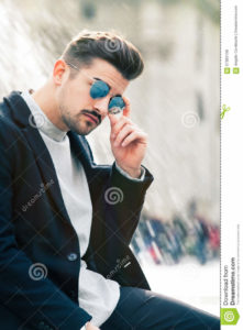 Cool handsome fashion young man. Stylish man in the city A charming young stylish man with sunglasses. Sitting position, confident attitude with setting in the historic city of Rome, Italy. Fashionable clothes.
