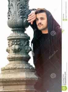 Gorgeous young man leaning against a old lamppost A handsome young man with hoodie is in the historic center of Rome, Italy. The boy is leaning against a pole of a streetlight. clean and youthful face. Beard. white background.