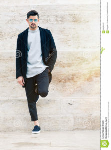 Handsome fashionable man, white wall A handsome young man with stylish sunglasses and fashionable clothes leaning against a marble wall white. Copyspace to the right