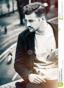 Handsome hairstyle young man city outdoors. Black and white Outdoor portrait of a handsome young man. Sunglasses in hand and stylish hair. Behind him a city street. Youth fashion. Black and white