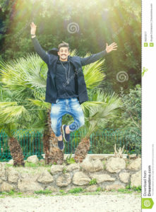 Happiness success of a young man outdoors. Jumping for joy A young and handsome man is jumping with joy, happiness and joy outdoor in a park. Smiling, with a modern look and stylish. Bright daylight.