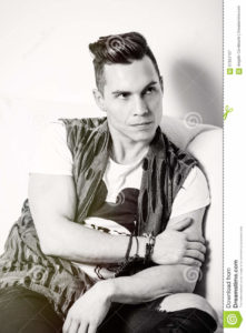 Portrait handsome man, stylish hair cut. Black and white A handsome young Italian man with trendy hair and cool clothing. He is sitting relaxed on a sofa.