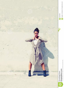 Rebellious confident woman. Rebellion female Young woman with a confident attitude. Standing in front of a worn and old wall. Rebellion, emancipation of women, power and strength concept. Clothing with long robe coat.