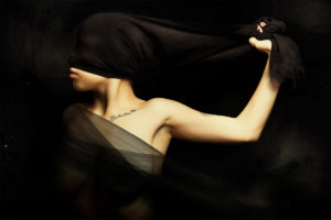 Artistic portrait. Woman blinded by a cloth hiding face. Rebellion and silence. A young woman is blinded by a cloth pulled from hand. artistic portrait with grunge background. A silk veil covering her breasts. Rebellion, silent, femininity, darkening, shame and women's empowerment concept.