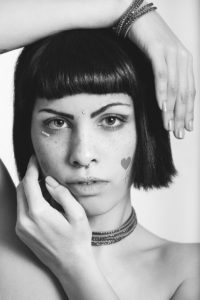 Portrait of young woman with freckles and heart-shaped stickers, bobbed hair. Hands geometric position. Black and white