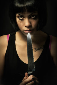 Young crying woman killer. Knife murder suicide. Crazy girl A young girl with problems is holding a big knife and points it in her mouth. Suicide, psychopathology murder concept. Black background
