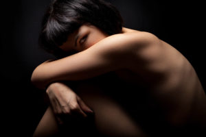 Naked girl, woman curled up in protection on black. Female health Young teenage girl in closed position to protect themselves. The young woman looking. Women 's health, personal care, female body care concept. Black background.