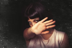 A young girl with her hand away and rejects violence of someone. Tears and crying. Black background. Focus on the face.