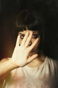 A young girl with her hand away and rejects violence of someone. Tears and crying. Black background. Focus on the eyes.