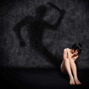 Violence against young woman. Girl and shadow. A small crying teenager is in a corner in a dark room. His shadow is about to hit it with violence. domestic violence, child abuse, violence against woman concept.