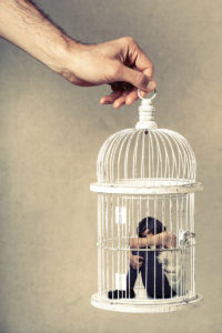 Violence against women. Woman in cage. Deprivation of liberty. Young woman locked in a cage. Young girl crouched position. A male hand holding the cage from above. Concept of deprivation of liberty and freedom of autonomy. Violence against woman and girls.