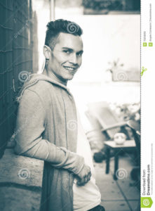 Vintage portrait. Young smiling man model hairstyle looking A handsome man is relaxed with his back to a low wall. Vintage retro colors. His gaze is happy and serene. The hair of the young man are fashionable.