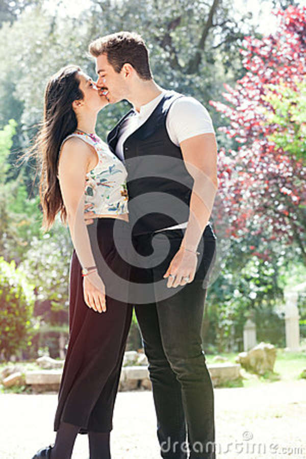 Beautiful couple embrace and kiss. Loving relationship and feeling. Outdoors A men and a women is strongly embrace with passion and feeling. Love affair between two young people. Behind them a natural park with trees and colorful foliage. Bright light that illuminates the scene.