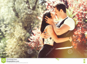 Beautiful couple embrace and love. Loving relationship and feeling. A men and a women is strongly embrace with passion and feeling. love affair between two young people. Behind them a natural park with trees and colorful foliage. Bright light that illuminates the scene.