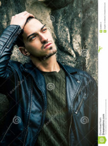 Beautiful young cool man with hand on head A cool guy posing outdoors with his hand on his head. Fashion rock style with leather jacket. Intense gaze.