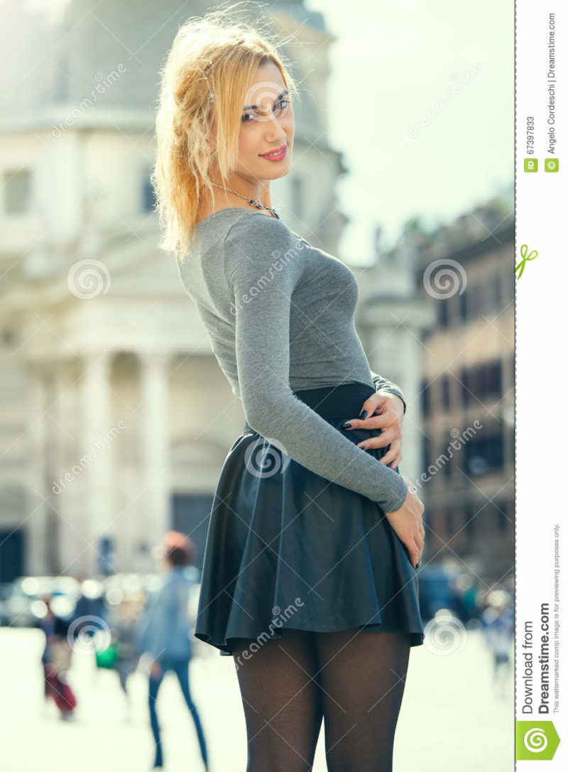 Blonde girl in the town, happily young tourist woman A beautiful young girl walks in the historic center of Rome in Italy. She is smiling, her look is trendy. Bright day and historical buildings in the background. Skirt and stockings.