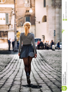 Girl walking on the street in the city wearing a skirt. Back. Girl walking on the street in the city. Back. Beautiful young girl walking in the historic center of Rome, Italy. Driveway with paving of cobblestones. Wearing a skirt