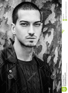 Man portrait outdoors. Handsome natural male. Black and white Portrait of a young handsome man near a tree. Intense gaze and eye-catching. Italian man. Tree with camouflage texture as background. Black and white