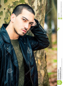Man portrait outdoors. Handsome natural male Portrait of a young handsome man near a tree. Intense gaze and eye-catching. Italian man