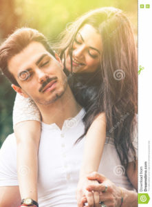 Passion and harmony. Relationship. Love and happiness. Passion and harmony. Relationship. Love and happiness. A smiling beautiful young women embracing her men from behind. Between the two there is a great harmony and joy. The men has a mustache and his eyes closed. Romantic atmosphere and bright outdoors in a natural park.