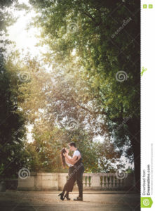 Young couple passion and love outdoor. Trees and nature. Natural love A beautiful young couple, men and woman, close to each other in a tight embrace. Love and deep passion. Feelings and relationship. The two are standing on a street with thick trees. A shaft of sunlight illuminates the scene.