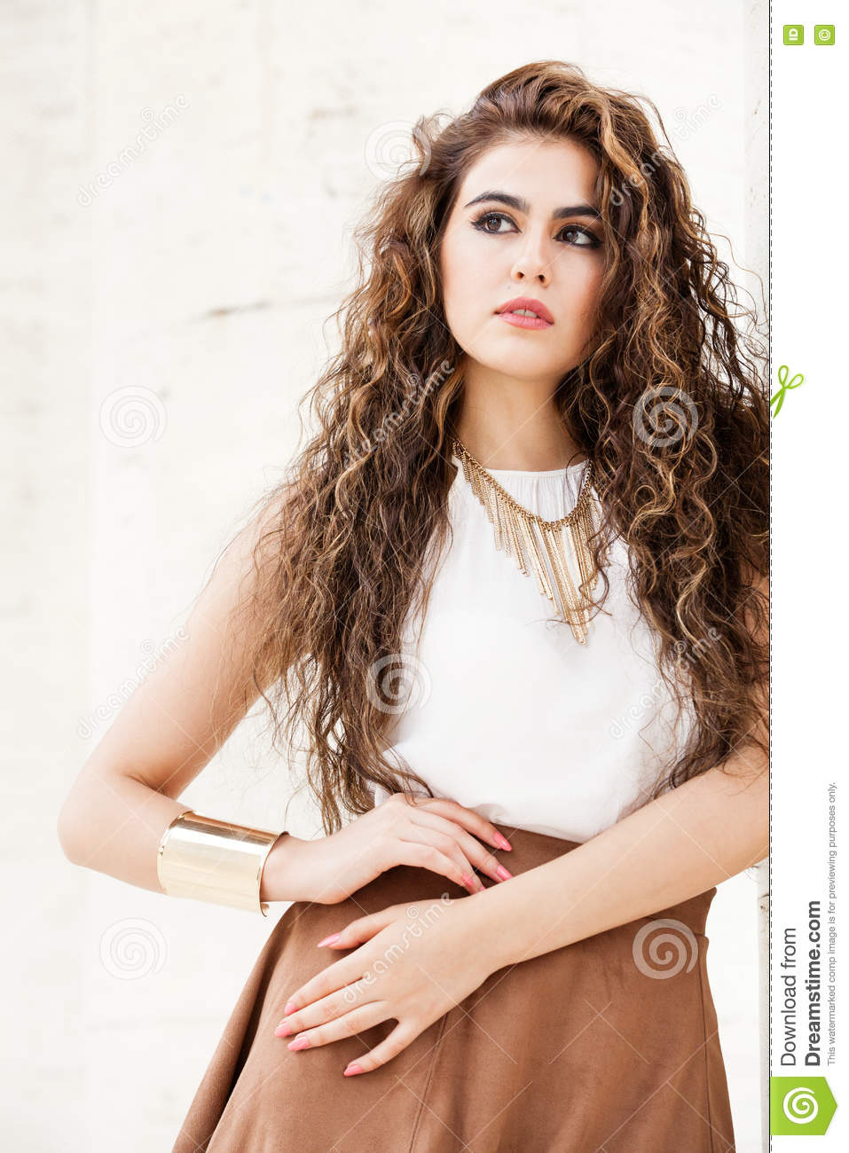 Beautiful woman with curly hair outdoor. Makeup A beautiful and happy young woman. Portrait of a girl with curly hair. Side look. Makeup on her face, perfect style. White sleeveless T-shirt, brown skirt, necklace and bracelet. Accessories. Sensuality, freshness, beauty and emotions.