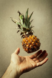 A nano pineapple flying over an open hand. Lightness of healthy food. Nature and man concept. Vintage background.