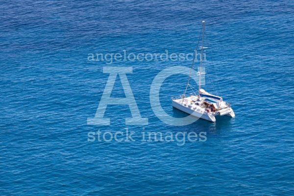Catamaran Boat White Color In The Middle Of The Blue Sea By Day. Angelo Cordeschi