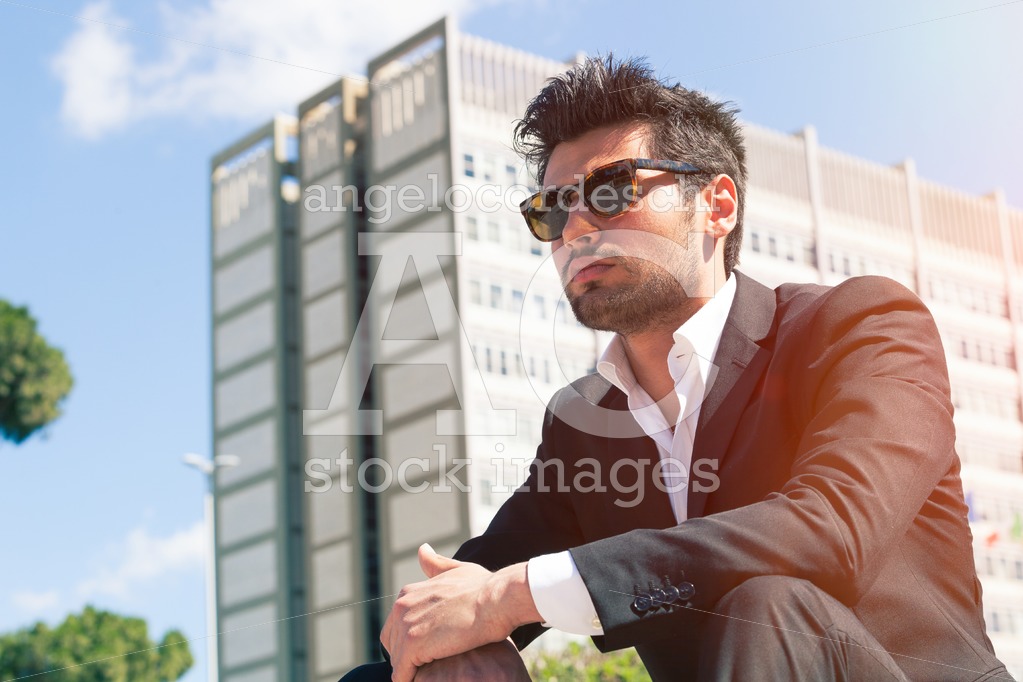 Confident Handsome Man With Sunglasses Sitting Outdoor. Building Angelo Cordeschi
