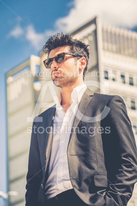 Confident handsome man with sunglasses standing outdoor, building behind him. - Angelo Cordeschi