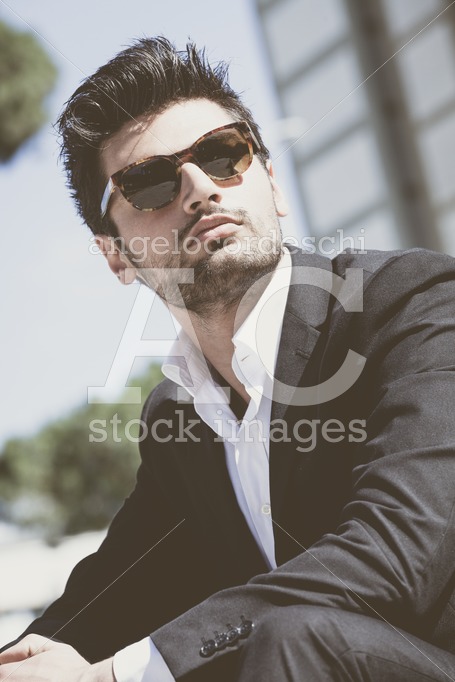 Confident young successful man sitting in the city. Wearing sunglasses, - Angelo Cordeschi