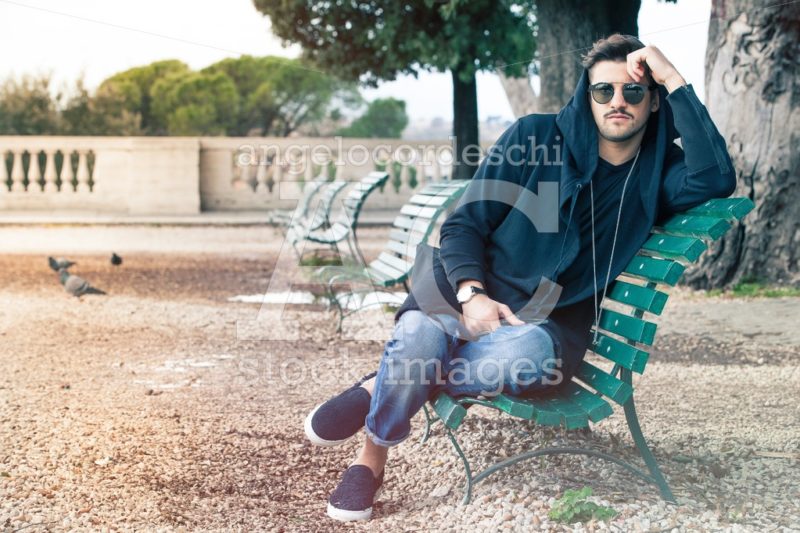 Fashionable Cool Young Man With Sunglasses Relaxing On A Bench. Angelo Cordeschi