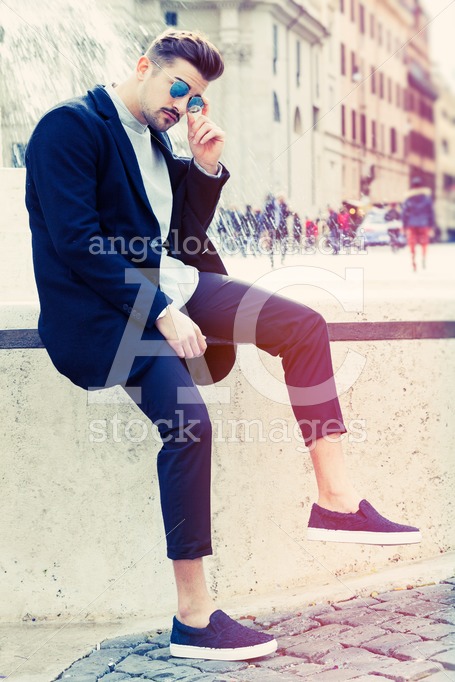 Handsome Fashionable Man Sitting And Posing On A Wall In The Str Angelo Cordeschi