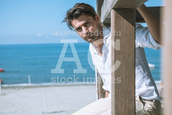 Handsome Man Relaxed At The Sea, Overlooking A Wooden Structure. Angelo Cordeschi