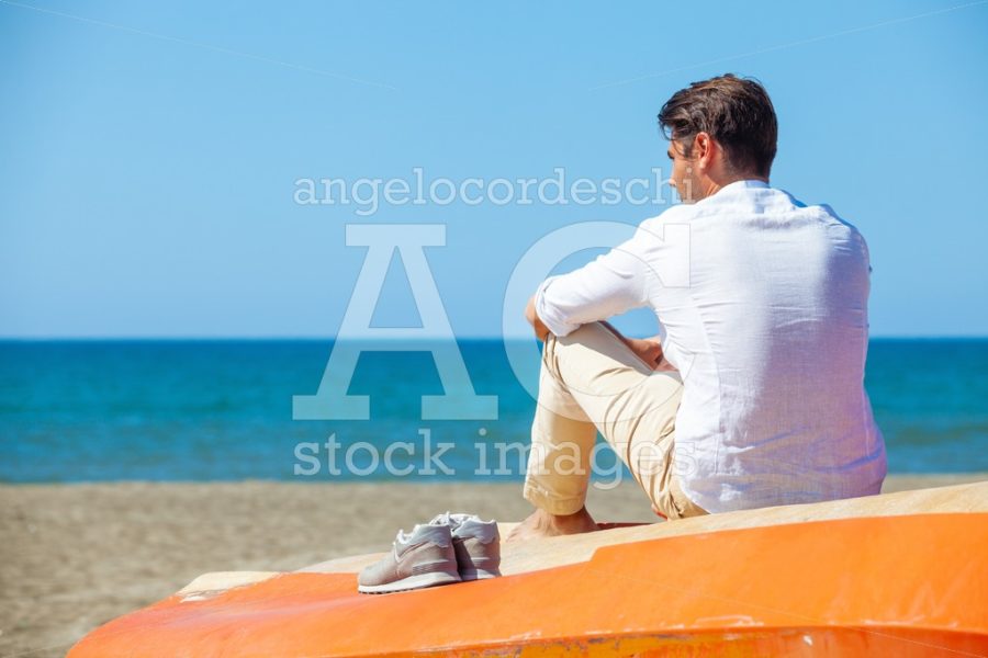 Lonely Man On The Beach Above A Boat Looking At The Sea. Angelo Cordeschi