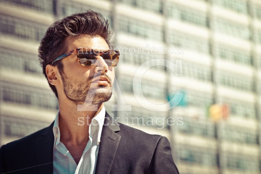 Man with sunglasses looking. Stubble beard. Building behind him. - Angelo Cordeschi