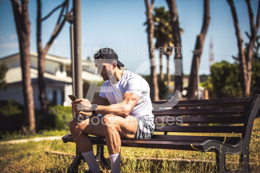 Sporty Man Personal Trainer Sitting Looking At His Phone On A Be Angelo Cordeschi