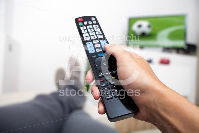 Watching TV. Remote control in hand. Watching football on TV. Ma - Angelo Cordeschi