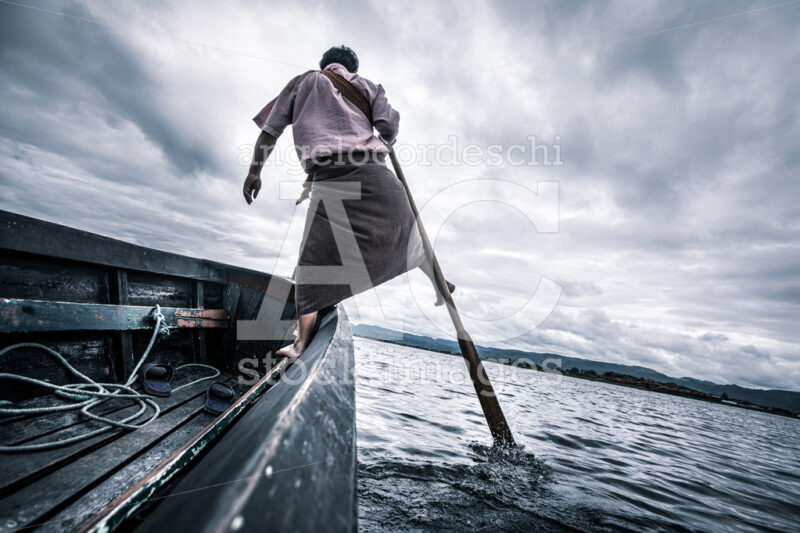 Burmese Fisherman Standing On His Boat Rowing With The Oar With Angelo Cordeschi